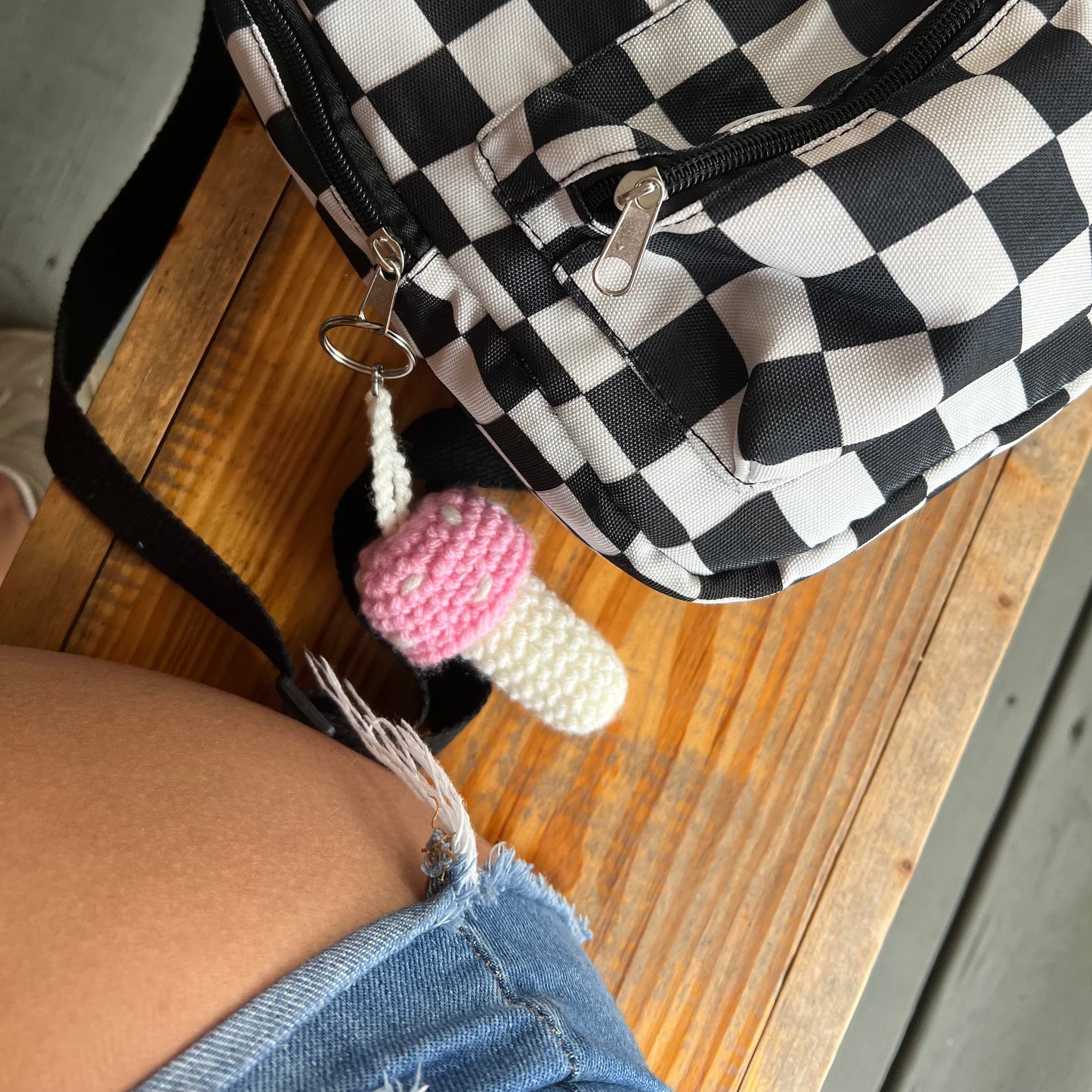 black and white checkered backpack with a pink and white mushroom keychain attached to the zipper