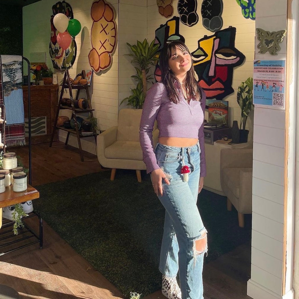 girl in a funky store wearing a crochet red and white mushroom keychain on her belt loop