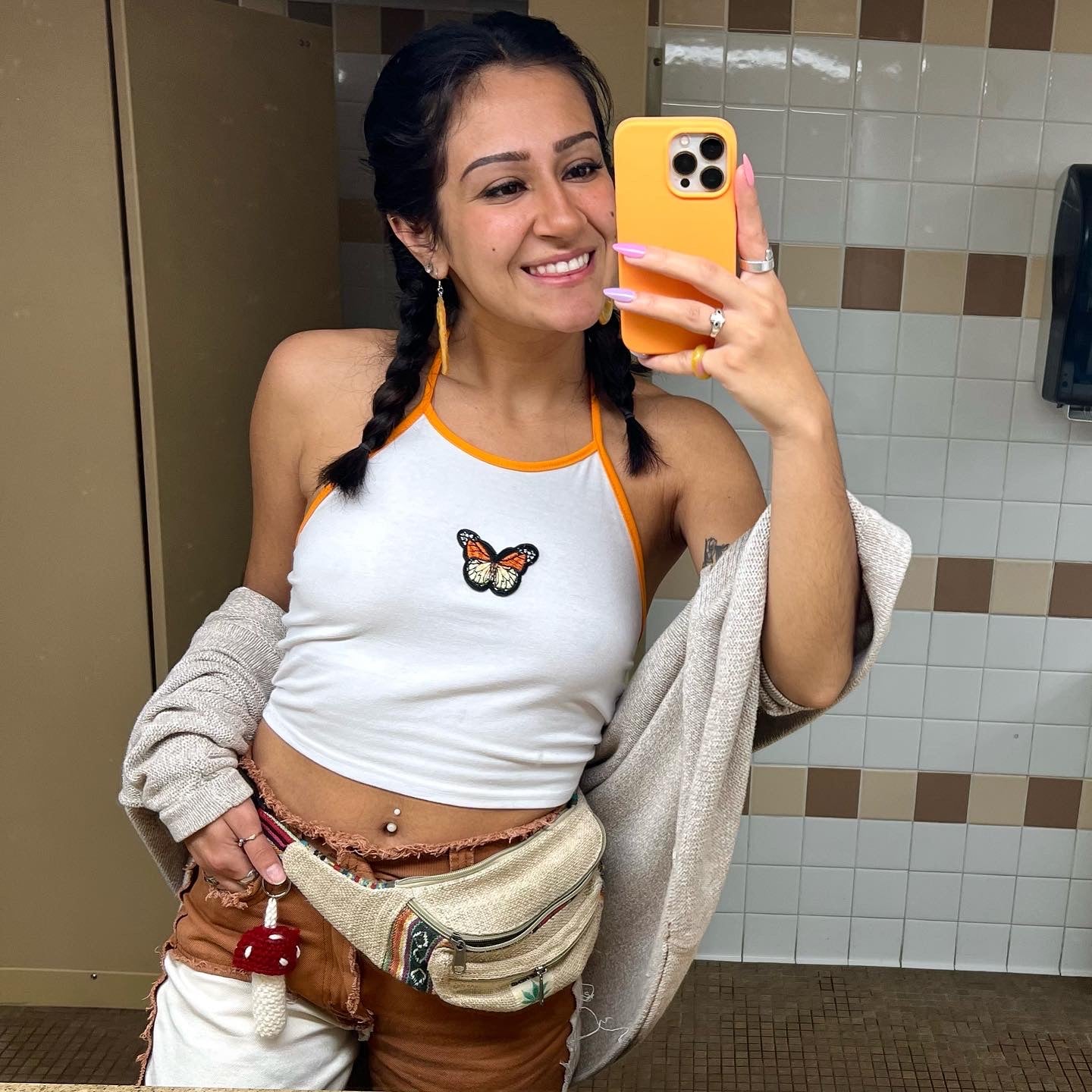 girl taking a mirror selfie of an outfit featuring a red and white crochet mushroom keychain